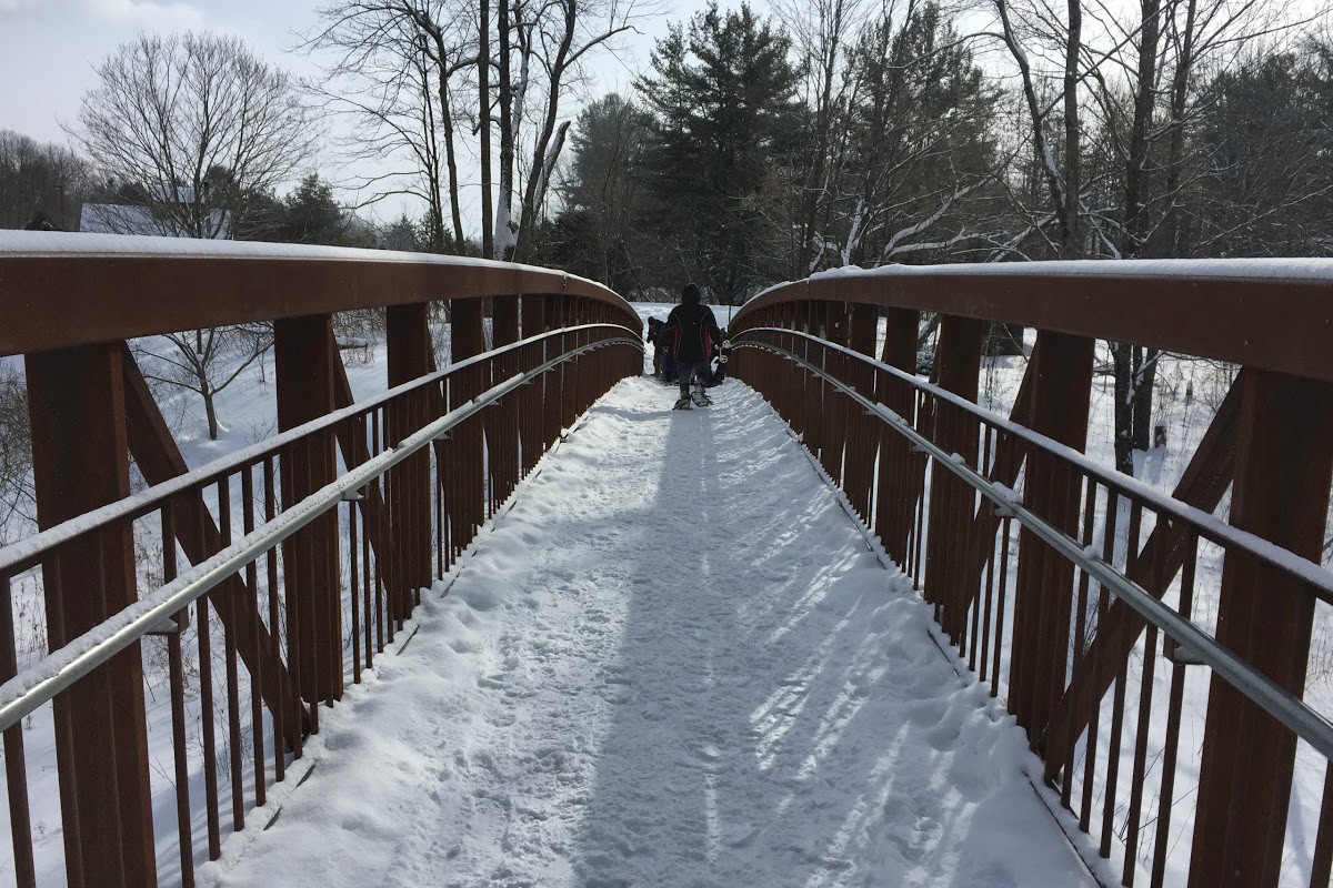 Man snowshoes across a bridge